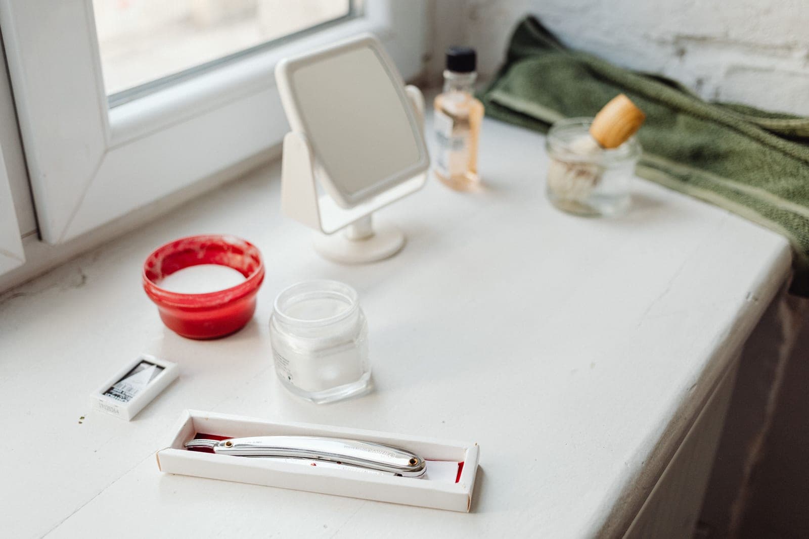A double-edge safety razor and a lathered shaving brush on a stone counter