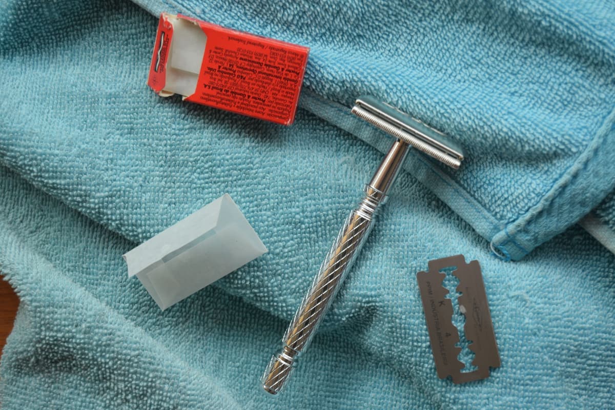 A chrome double-edge safety razor lying on a stone bathroom surface